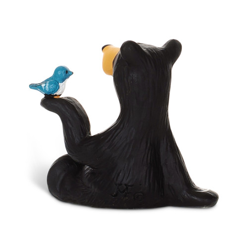 Back view of a small figurine of a black bear holding a small blue bird on its paw.