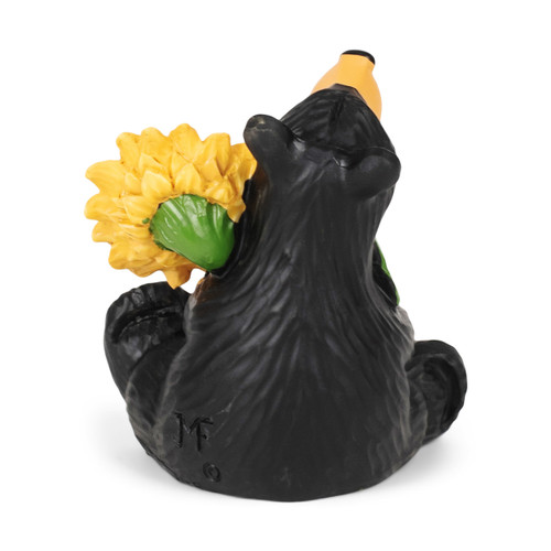 Back view of a sitting black bear figurine holding a large yellow sunflower with a green stem and leaves.