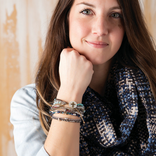 Bracelet with seven strands consisting of pearls, gemstones, and glass beads is multi-colored. Large silver pendant with gold cross on bracelet. Model is wearing bracelet on her wrist