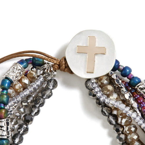 Bracelet with seven strands consisting of pearls, gemstones, and glass beads is multi-colored. Large silver pendant with gold cross on bracelet. View is focused on the pendant