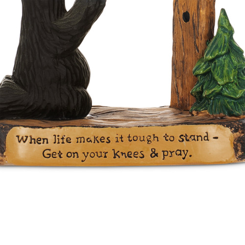 Detail view of the saying on a black bear figurine kneeling in prayer before a wood cross. The base says "When life makes it tough to stand - Get on your knees & pray".