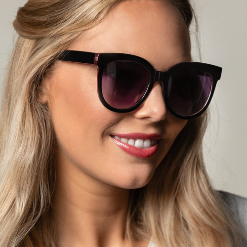 A close up image of a woman in a gray shirt wearing black sunglasses.