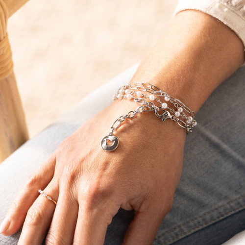 Close up of a silver chain and bead bracelet on a woman's wrist that has a round silver charm with a dove cutout.