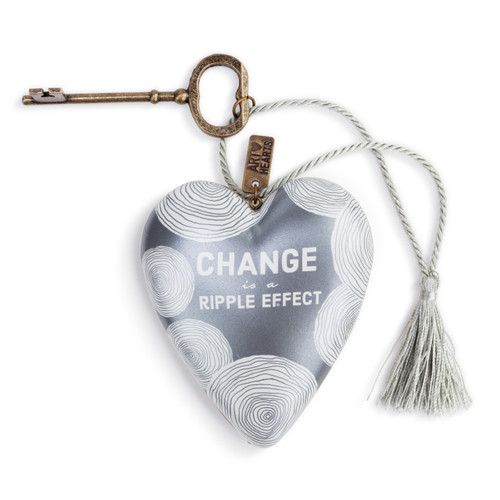 A deep silver blue art heart with white circular patterns, and reads "Change is a ripple effect" in white lettering. With a bronze key and silver tassel.