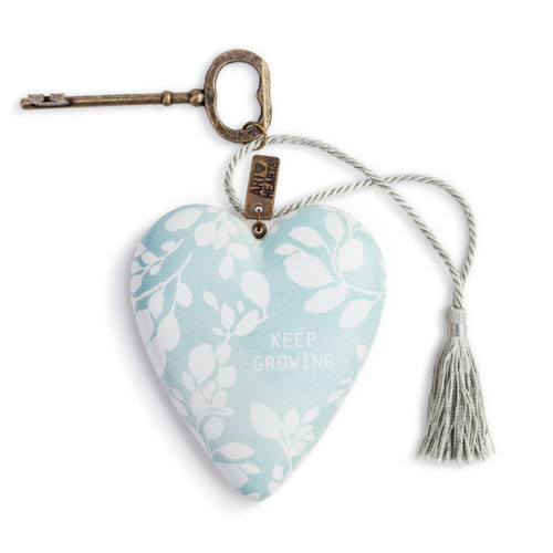 A light blue art heart with a white floral print and reads "keep going" in white typography. With a bronze key and silver tassel.