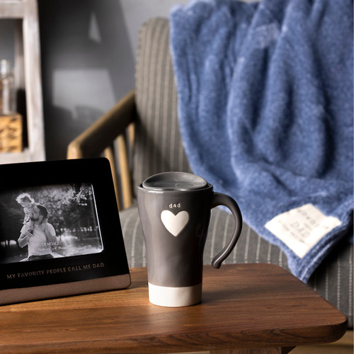 A living room display of Dad themed items such as a blue blanket, a gray travel mug and a black ceramic photo frame.