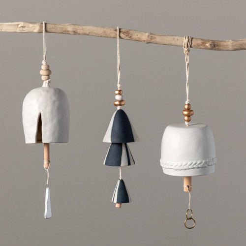 A close up image of three bells hanging from a single wooden branch. All differing shapes, textures, and colors (black, white and gold).