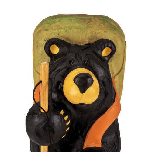 Detail view of the face on a large black bear figurine wearing a light green backpack and holding a tall walking stick.