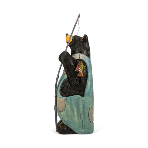 Left profile view of a large black bear figurine wearing light blue overalls and holding a wood fishing pole with a small fish on the hook.