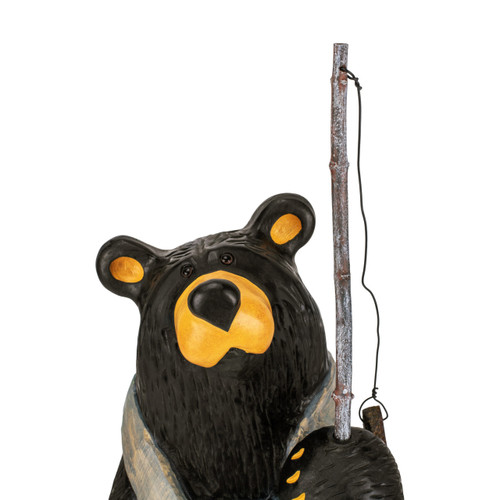 Detail view of the face on a large black bear figurine wearing light blue overalls and holding a wood fishing pole with a small fish on the hook.