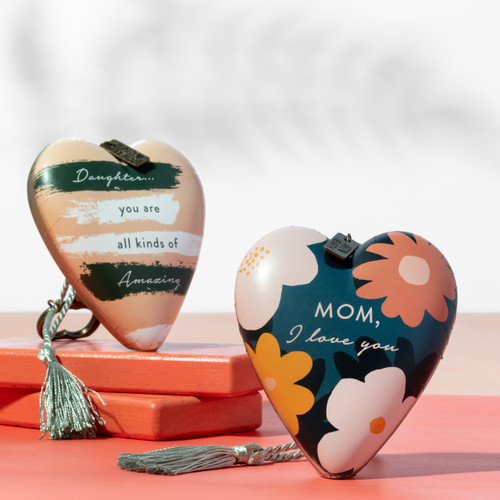 A floral heart sculpture that says "Mom, I love you" and another heart with a daughter theme, both with a gold key and silver tassel.