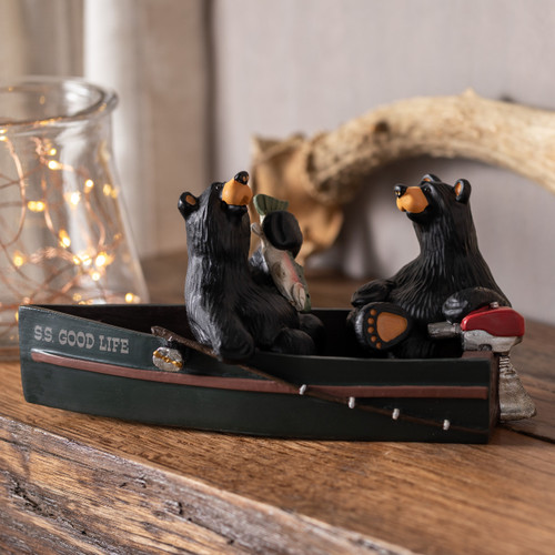 A dark, textured, wooden mantle topped with a jar of lights, an antler, and a figurine of two black bears sitting in a black fishing boat, one bear holding a fish.