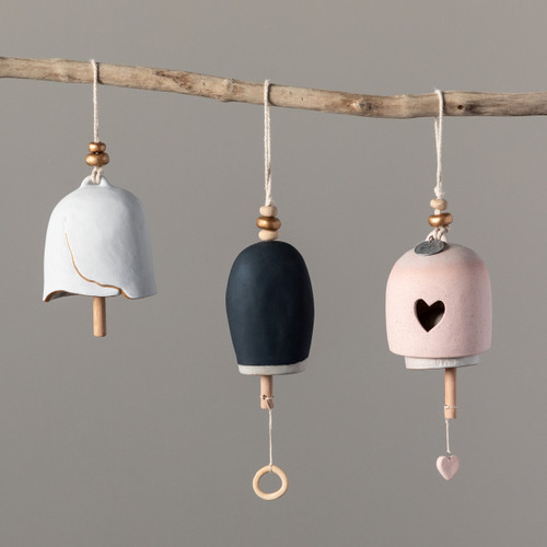 A close up image of three bells hanging from a single wooden branch. All differing shapes, textures, and colors (pink, black, and white).