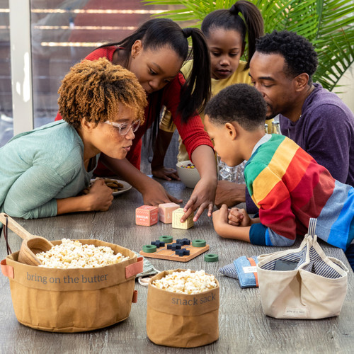 A family gathered around a wood picnic table playing a dice game together surrounded by snacks.