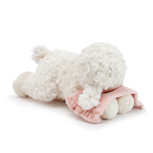 A right facing view of a plush, white laying lamb with a simple pink heart on its paw. Holding a soft pink blanket with a silver cross.