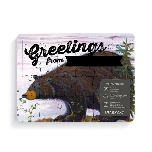 A 24 piece wood postcard puzzle with a bear sniffing huckleberries that says "Greetings from..." with room for personalization, with a product information tag attached.