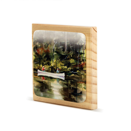 A square wood plaque angled to the left with a tile attached that has a watercolor image of a canoe on the water.