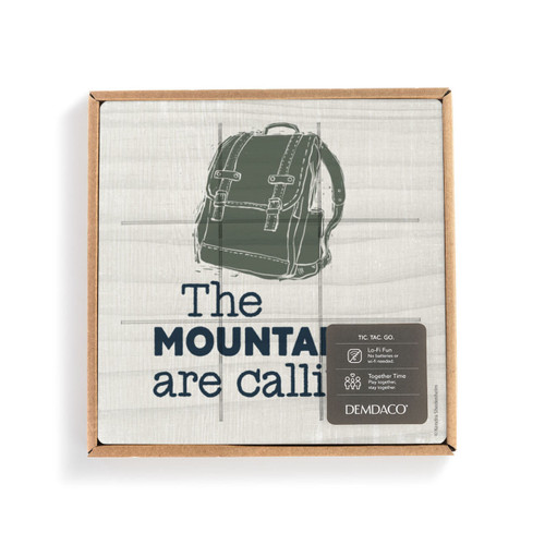 A light square board with a green backpack and the saying "The Mountains are calling" with lines for tic tac toe, in a packaging box with a product information tag.