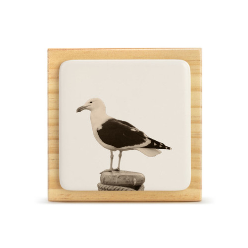 A square wood plaque with a white tile that has an image of a sea gull.