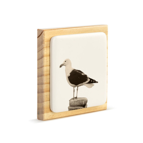 A square wood plaque with a white tile that has an image of a sea gull, displayed angled to the right.