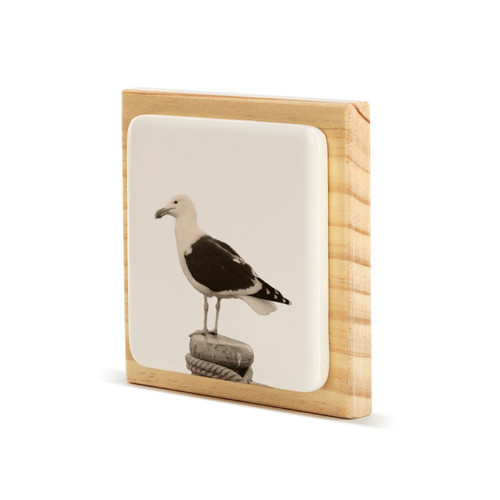 A square wood plaque with a white tile that has an image of a sea gull, displayed angled to the left.