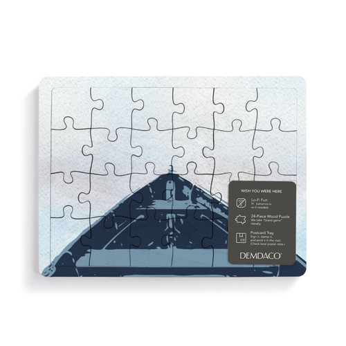 A rectangular wood 24 piece postcard puzzle with the bow of a boat on a light background with a product information tag attached.
