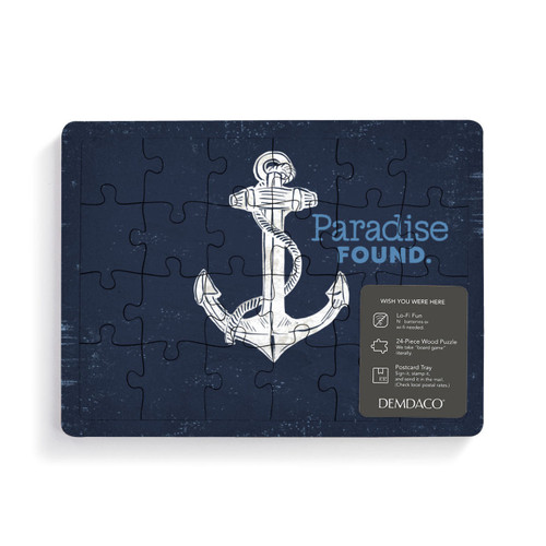 A rectangular wood 24 piece postcard puzzle of a white anchor on a dark blue background and the saying "Paradise Found" with a product information tag attached.