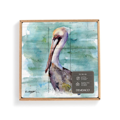 A square wood tic tac toe board with a watercolor image of a pelican, displayed in a packaging box with a product information tag.