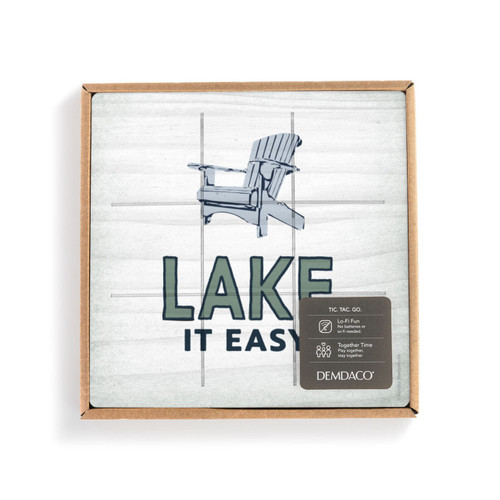 A white square board with a blue Adirondack chair and the saying "Lake it Easy" with lines for tic tac toe in a packaging box with a product information tag.