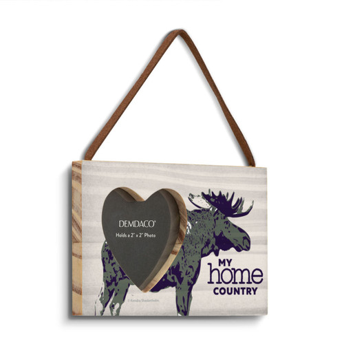 A rectangular wood hanging frame with a 2 inch heart shaped opening for a photo that has a moose on a light background that says "My home country" angled to the right.