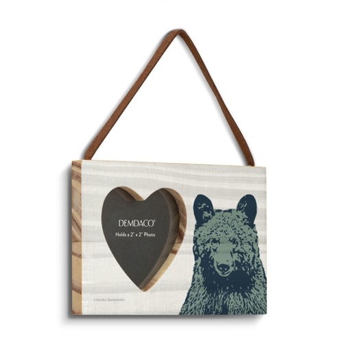 A hanging wood rectangular frame with a 2 inch heart shaped opening for a photo next to an image of a bear's head shown angled to the right.