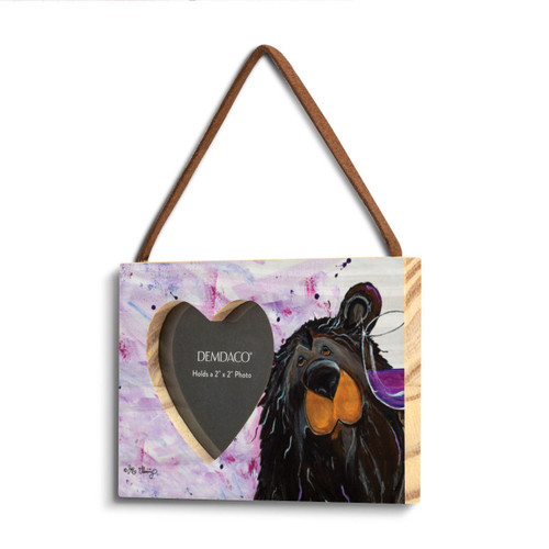 A rectangular wood hanging frame with a 2x2 inch heart shaped photo opening and has a painted image of a black bear holding a glass of wine, displayed angled to the left.