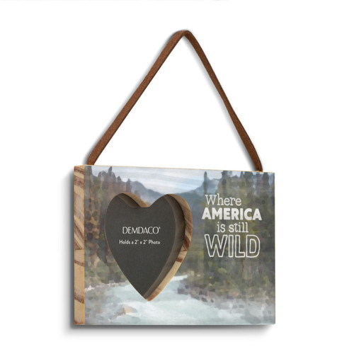 A rectangular wood hanging ornament with a 2 inch heart shaped opening for a photo next to the saying "Where America is still Wild" on a mountain stream background, displayed angled to the right.