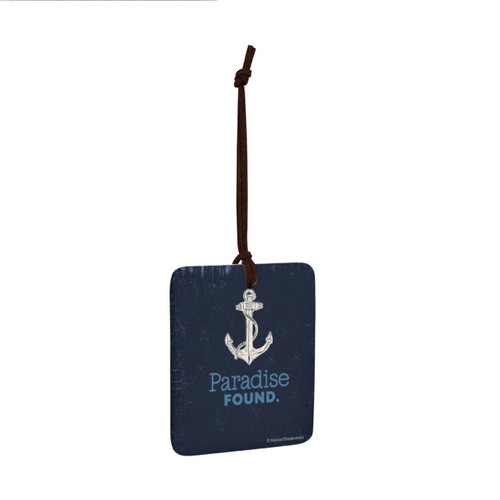 A square hanging ornament with a white anchor that says "Paradise Found" on a dark blue background angled to the right.