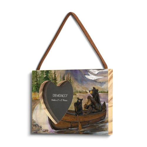 A rectangular wood hanging frame with a 2x2 inch heart shaped photo opening and has a painted image of two black bears rowing a canoe, displayed angled to the left.
