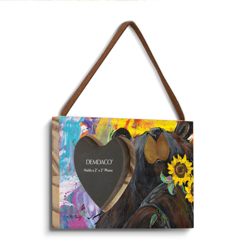 A rectangular wood hanging frame with a 2x2 inch heart shaped photo opening and has a painted image of a black bear holding sunflowers, displayed angled to the right.