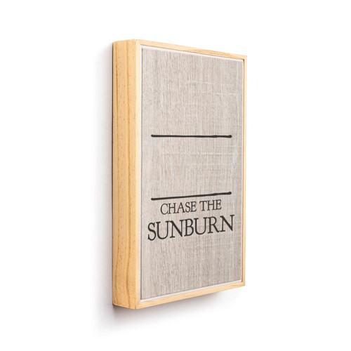 A light wood framed wall art that says "Chase the Sunburn" on a wood grain background under two black lines for personalization, displayed angled to the right.