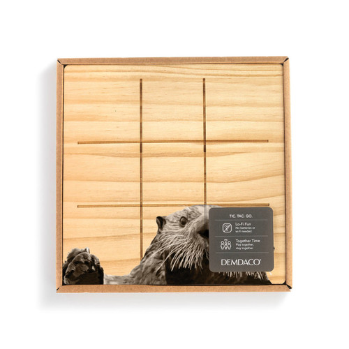 A square wood board for tic tac toe with an image of an otter, shown in a packaging box with a product information tag.