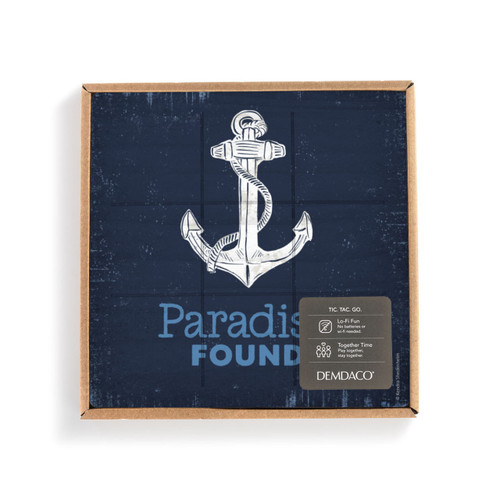 A dark blue square board with a white anchor and the saying "Paradise Found" with lines for tic tac toe, in a packaging box with a product information tag.
