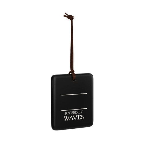 A square black hanging ornament that says "Raised by Waves" in white under two white lines with room for personalization, displayed angled to the right.
