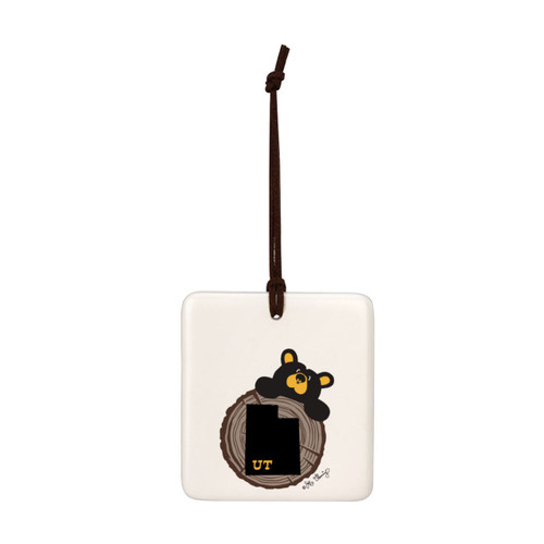 A white square hanging ornament with a black bear peeking over a tree stump with Utah on it.