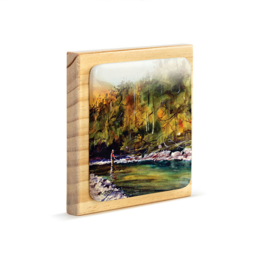 A square wood plaque angled to the right with a tile attached that has a watercolor image of a fly fisher in a river.