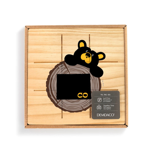 A square wood tic tac toe board with a black bear looking over a tree stump with Colorado on it, displayed in a packaging box with a product information tag.
