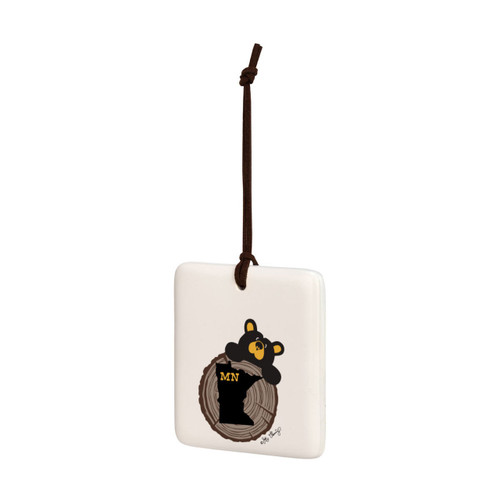 A white square hanging ornament with a black bear peeking over a tree stump with Minnesota on it, displayed angled to the left.