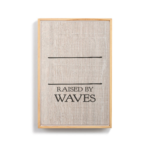 A light wood framed wall art that says "Raised by Waves" on a wood grain background under two black lines for personalization.