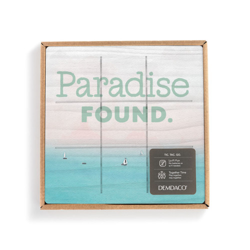 A square wood board for tic tac toe with a lake scene that says "Paradise Found" in a packaging box with a product information tag.