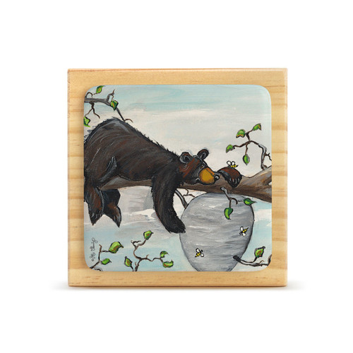 A square wood plaque with an attached painted tile of a black bear on a branch next to a beehive.