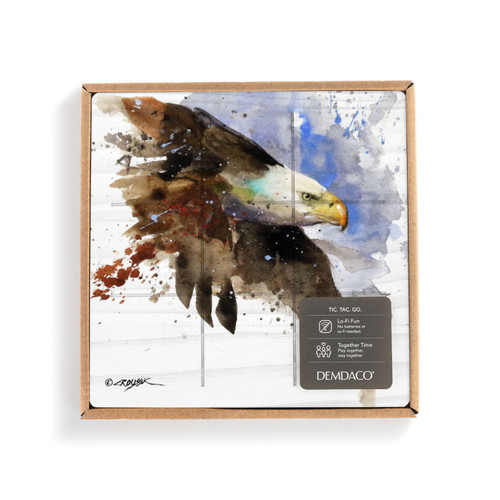 A square wood tic tac toe board with a watercolor image of a bald eagle in flight, displayed in a packaging box with a product information tag.