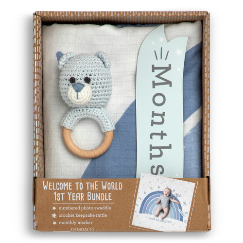 A gift set including a large blue and white sign with the months printed on it, a light blue knit bear rattle on a wood ring and a sign that says "months", displayed in a packaging box.