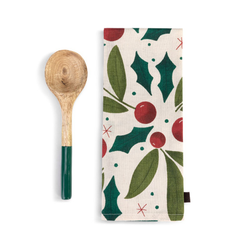 A cream kitchen towel with holly leaves and red berries next to a wood spoon with a green handle.